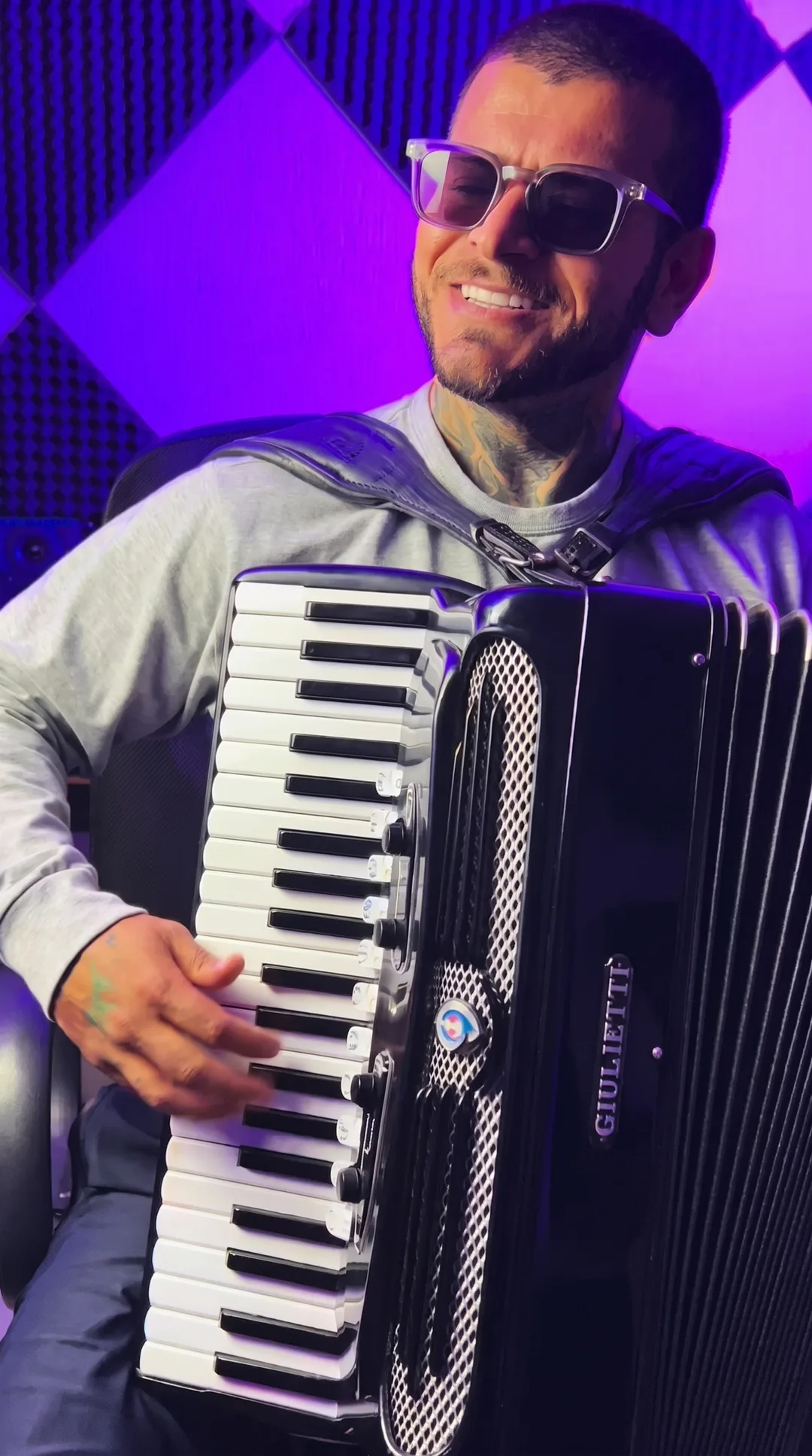 Clayton Gama sorrindo com a sanfona no estúdio, sob luz roxa