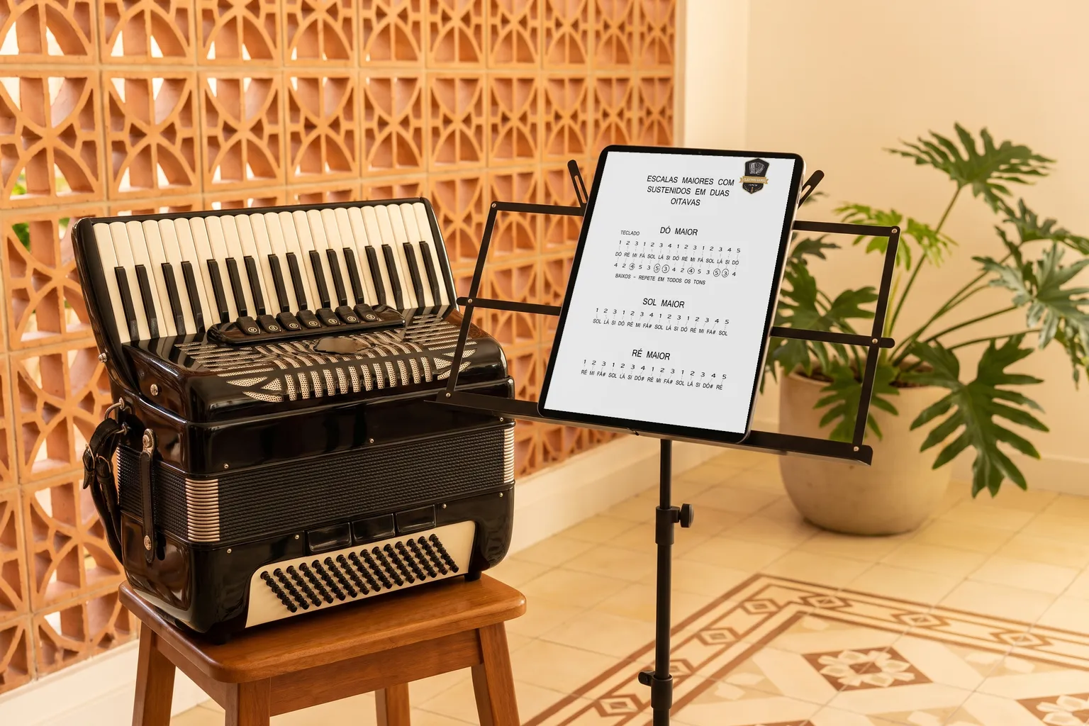 Tablet numa estante de partitura mostrando a página de escalas do e-book, ao lado de uma sanfona num banco de madeira, com parede de cobogó ao fundo