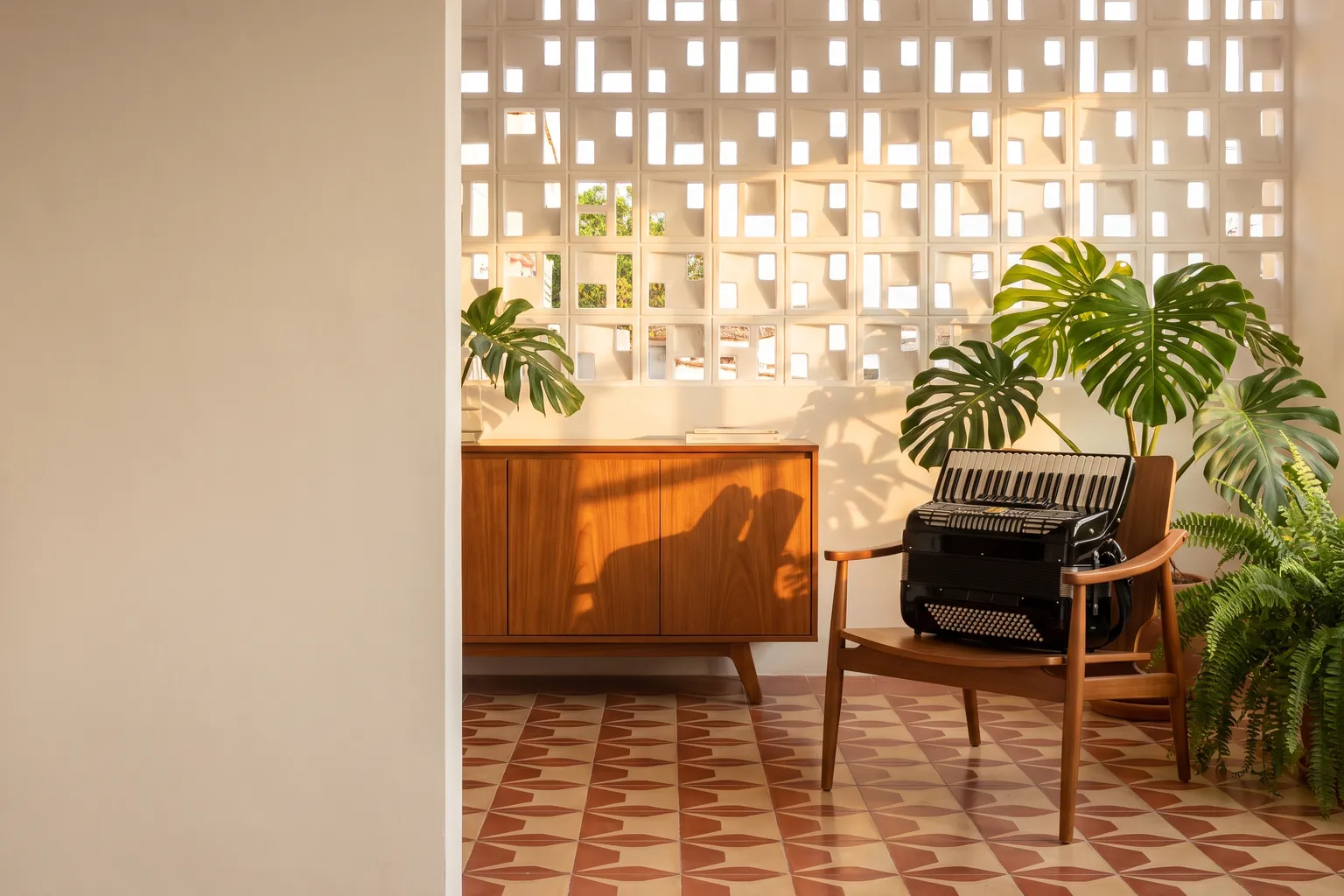 Sala de uma casa contemporânea com parede de cobogó, aparador de madeira e uma sanfona nova numa poltrona